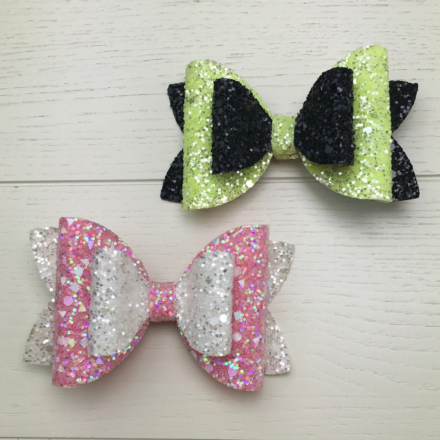 Two glittery hair bows on a light wooden surface
