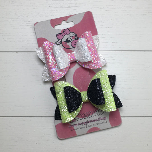 Two glittery hair bows on a display card with a Maggie Moo logo on a light wooden surface