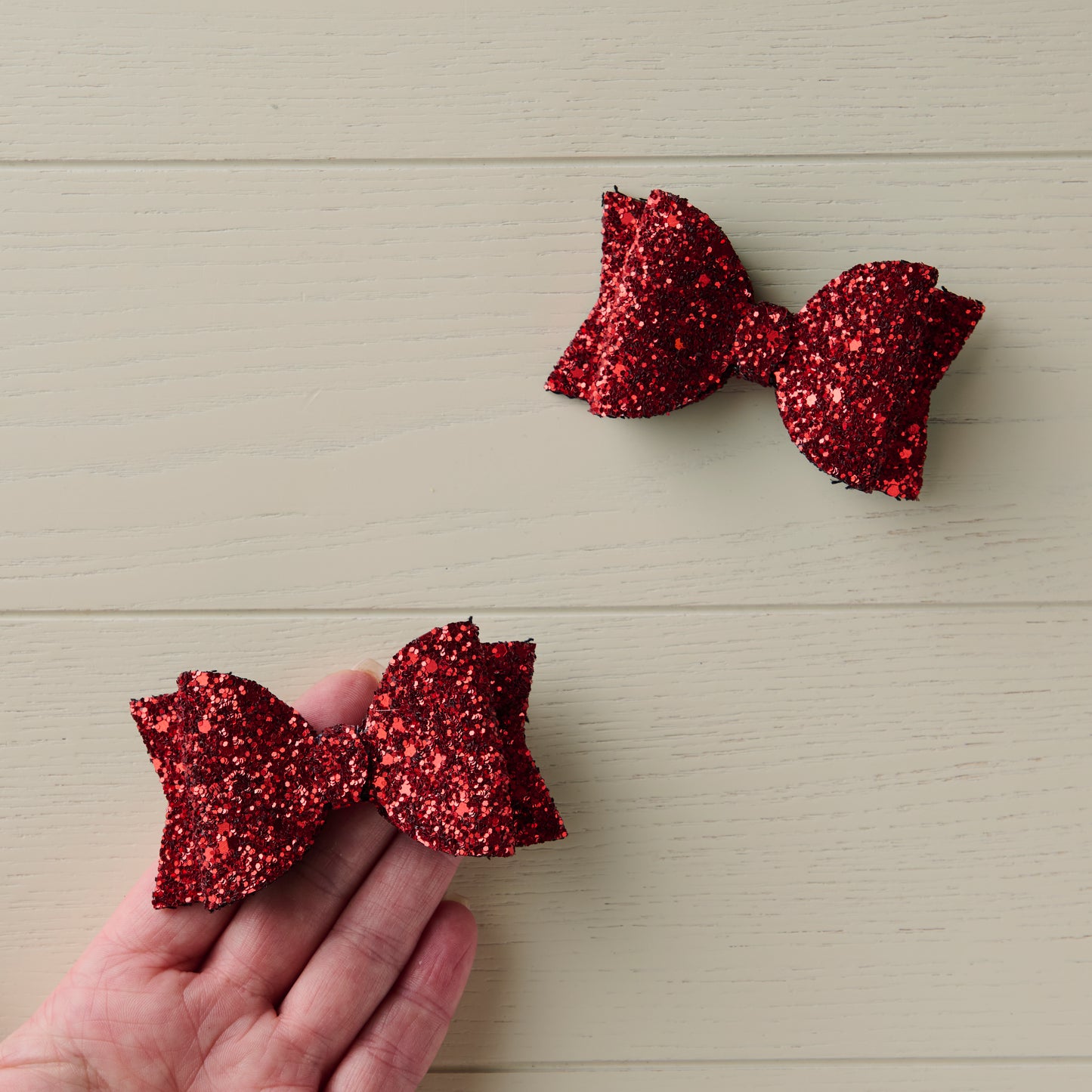 a photo showing two red glitter hair bows, one of them on a palm of a hand for size reference