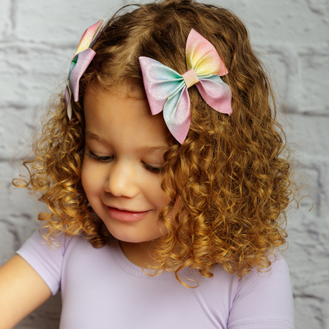 a girl with curly hair wearing two rainbow glitter hair bows