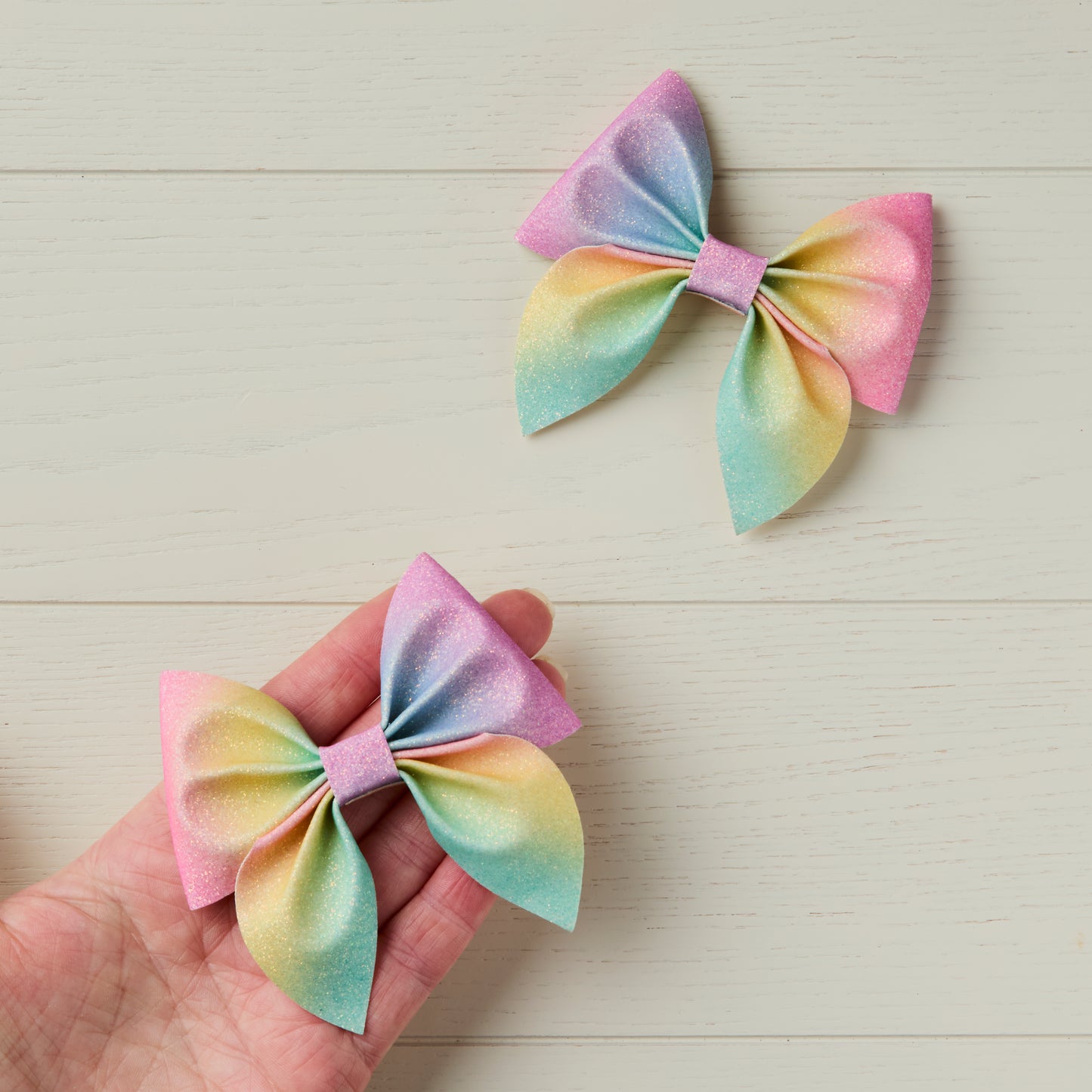 two bows on light wooden background, one of the bows shown on top of a palm of a hand for size reference