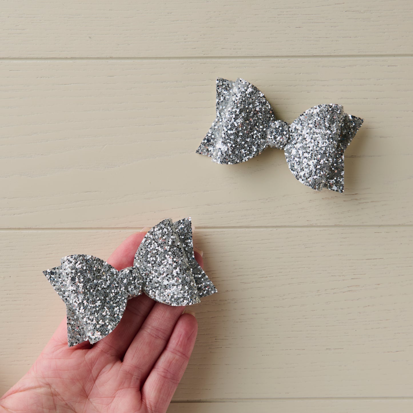 two glitter bows in silver, one shown on a palm of a hand for size reference