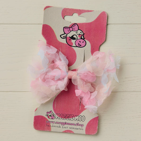 Pink hair bow with 3D floral details on a display card with a cute cow logo against a light wooden background
