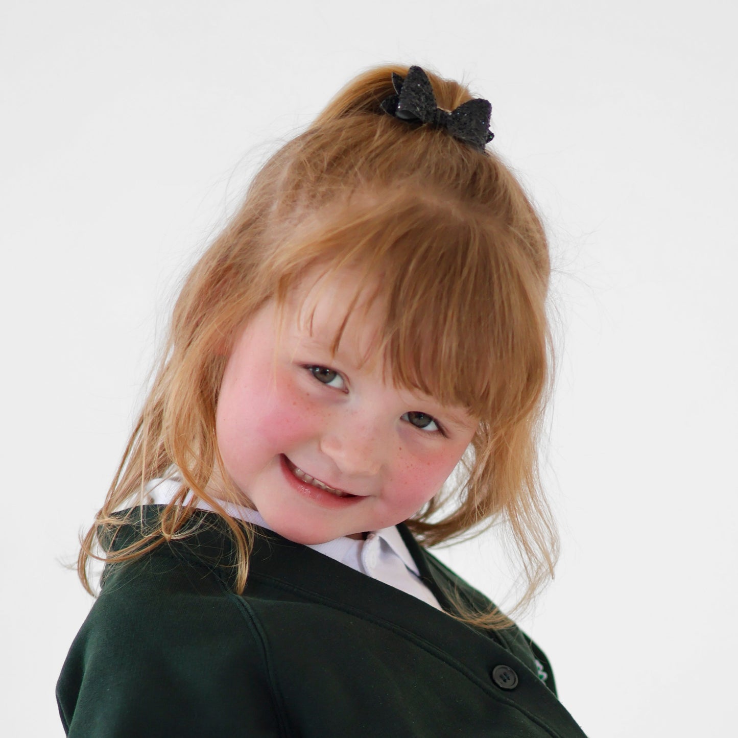 Young girl wearing a dark green school cardigan and sparkly black glitter bow clipped to a ponytail