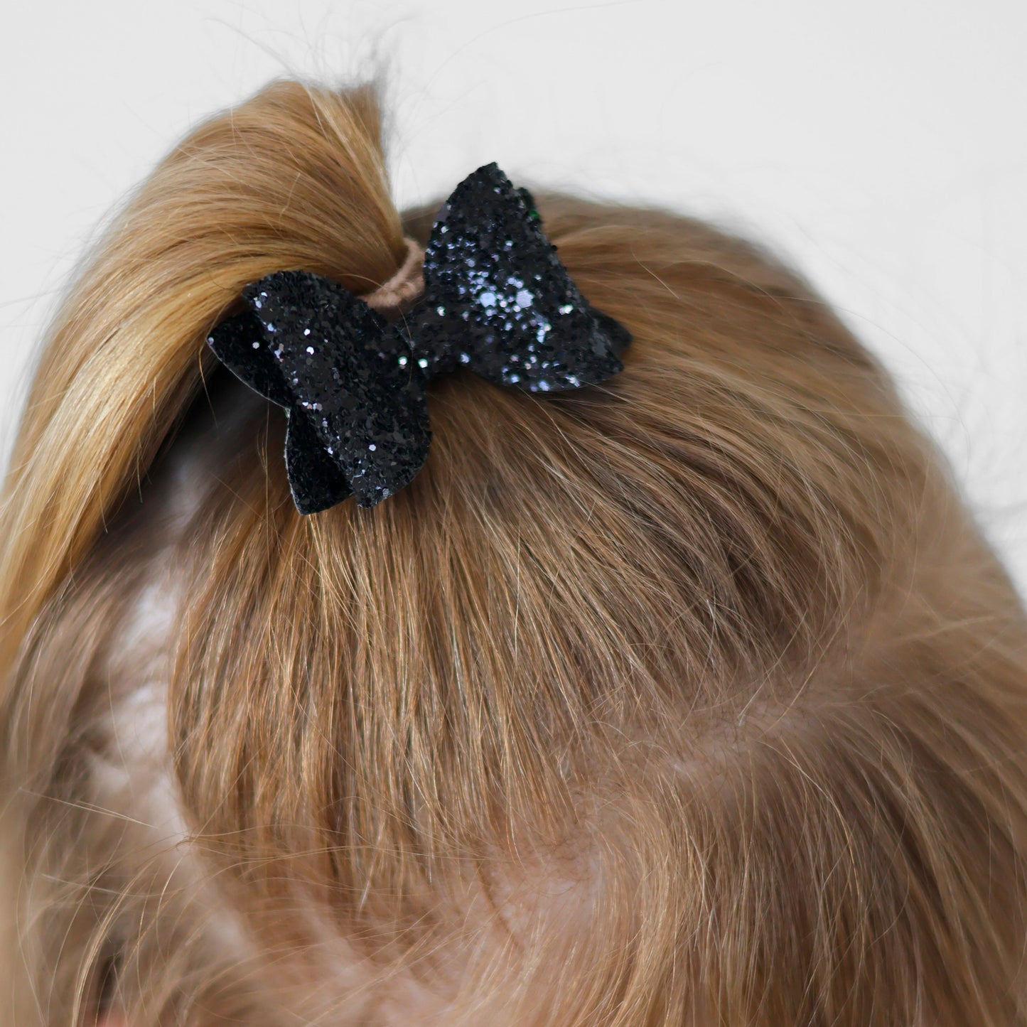 Close-up of a child wearing a black glittery hair bow clipped to her ponytail against a white background