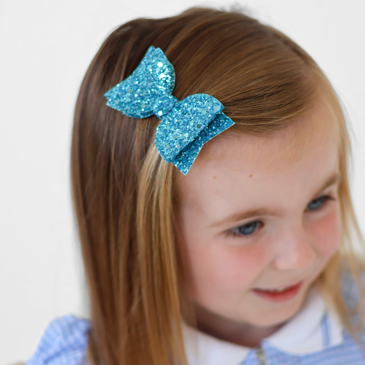 a close up of a blue glitter hair bow worn as a side clip by a young girl