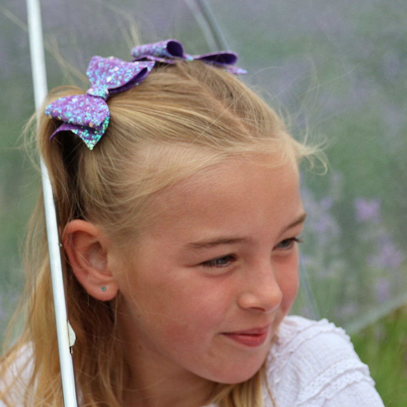 A young girl with purple hair bows under a transparent umbrella in a lavender field.