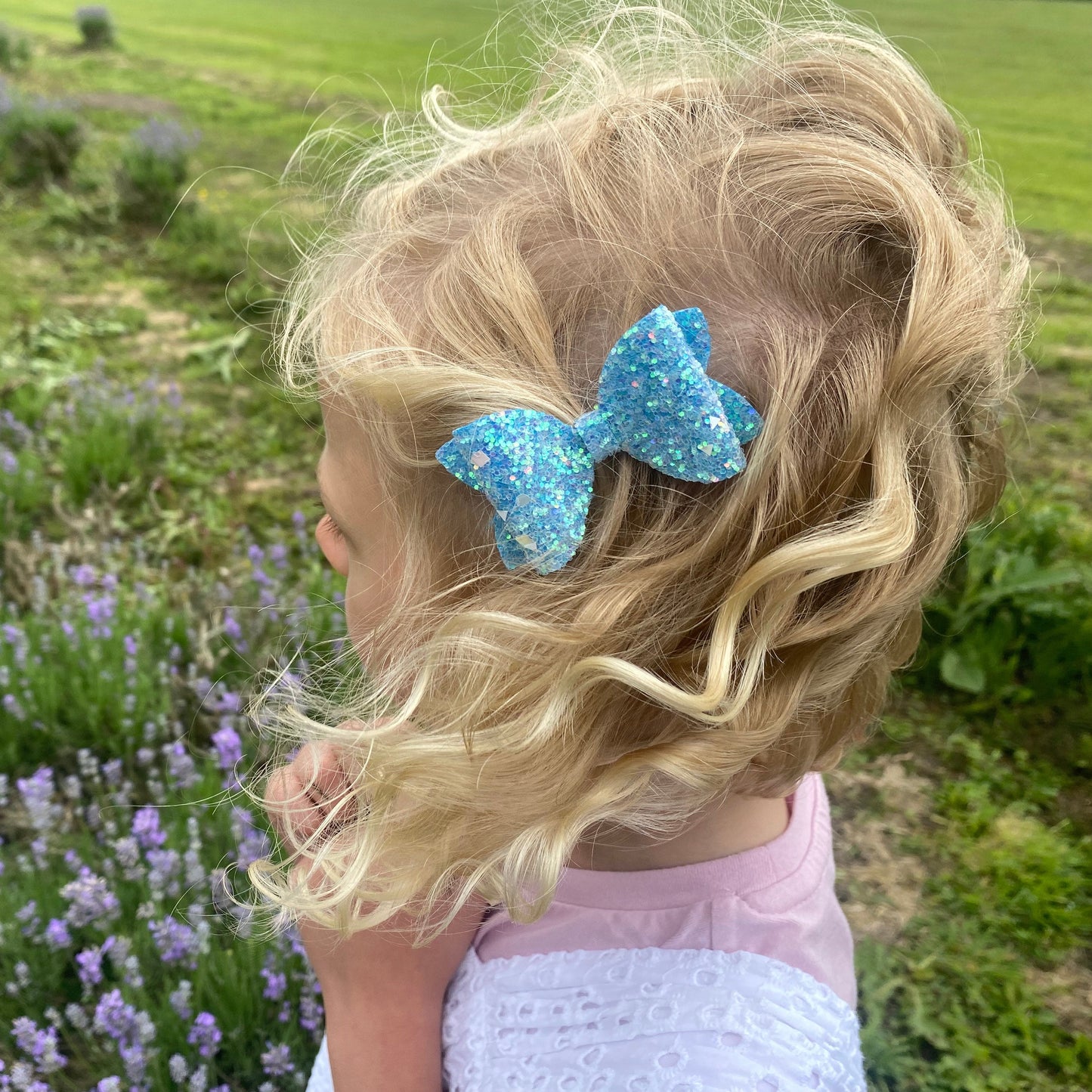 Child with a blue hair bow standing in a lavender field