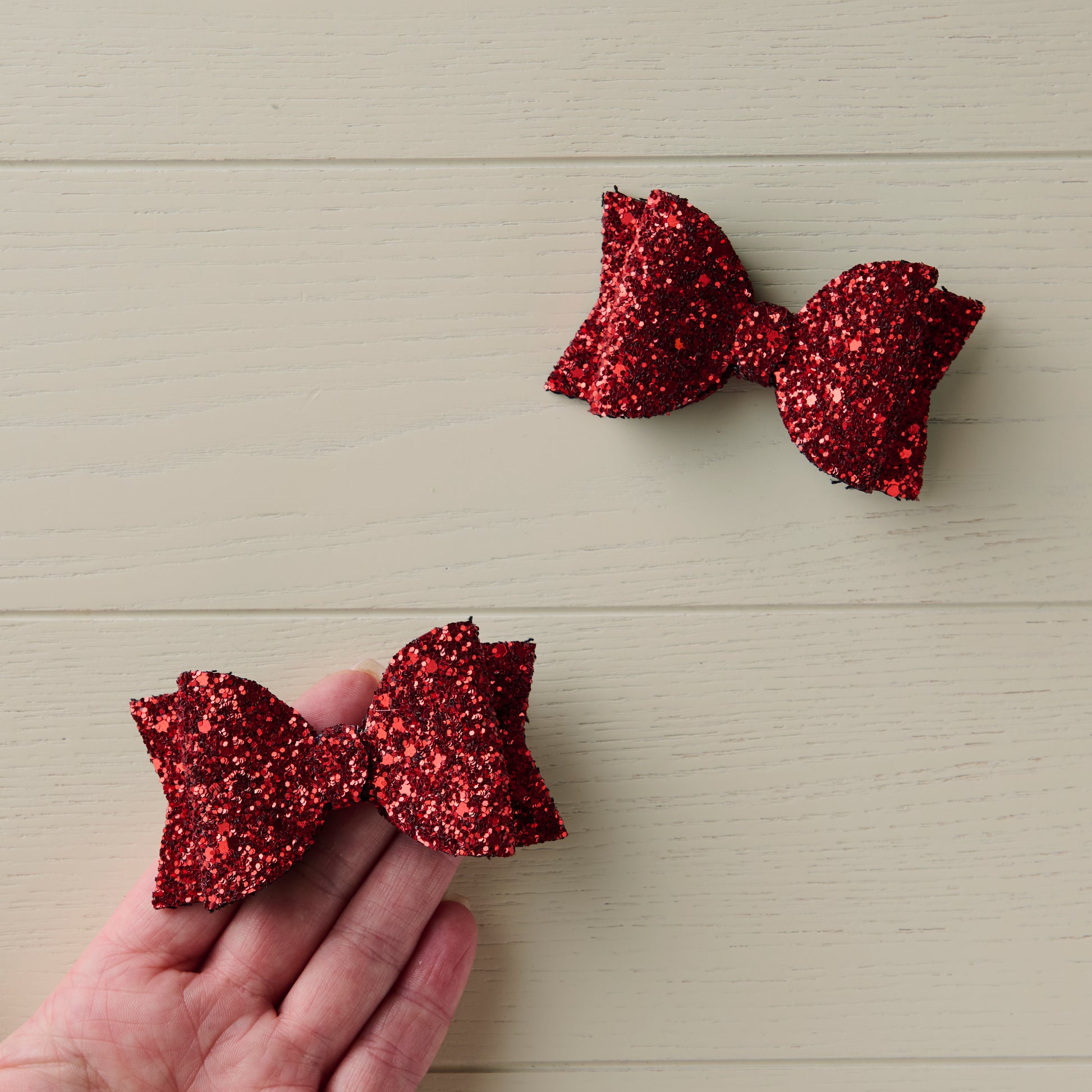 a photo showing two red glitter hair bows, one of them on a palm of a hand for size reference