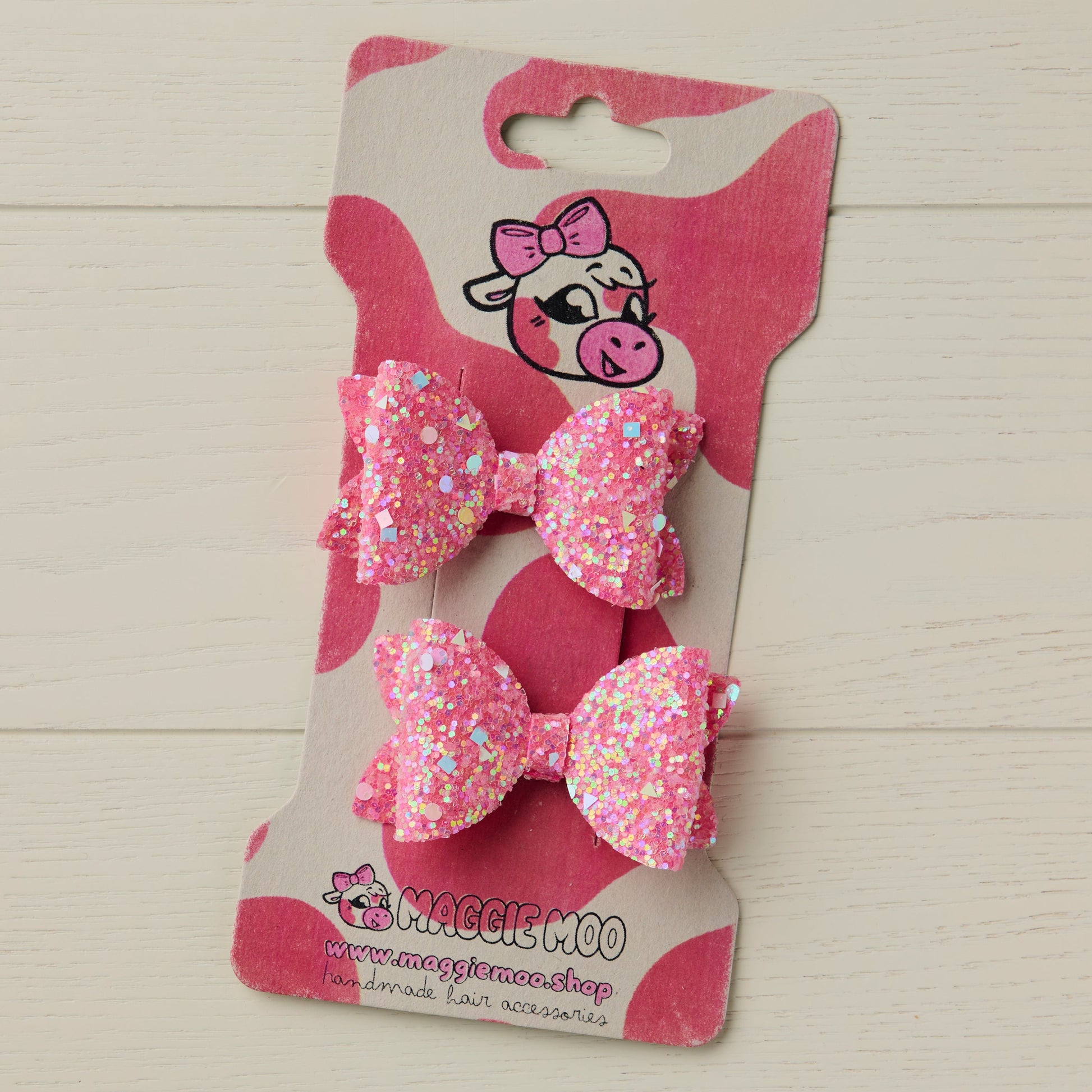 Two sparkly pink hair bows on a display card with a cute cow logo