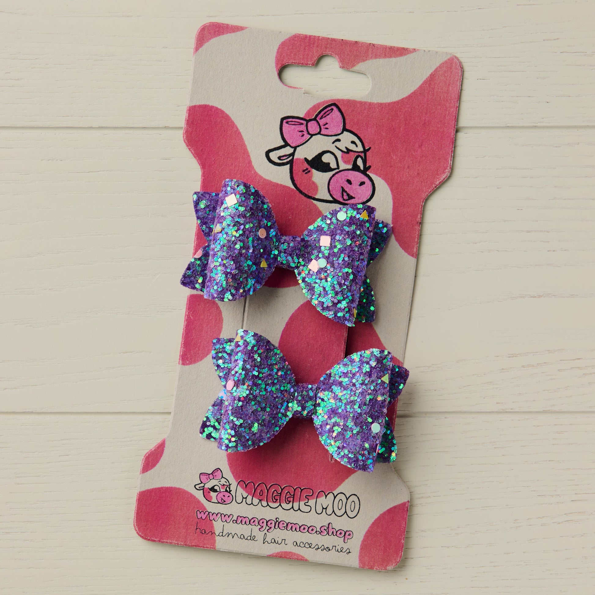 Two chunky glitter hair bows clipped onto a display card with a cow logo