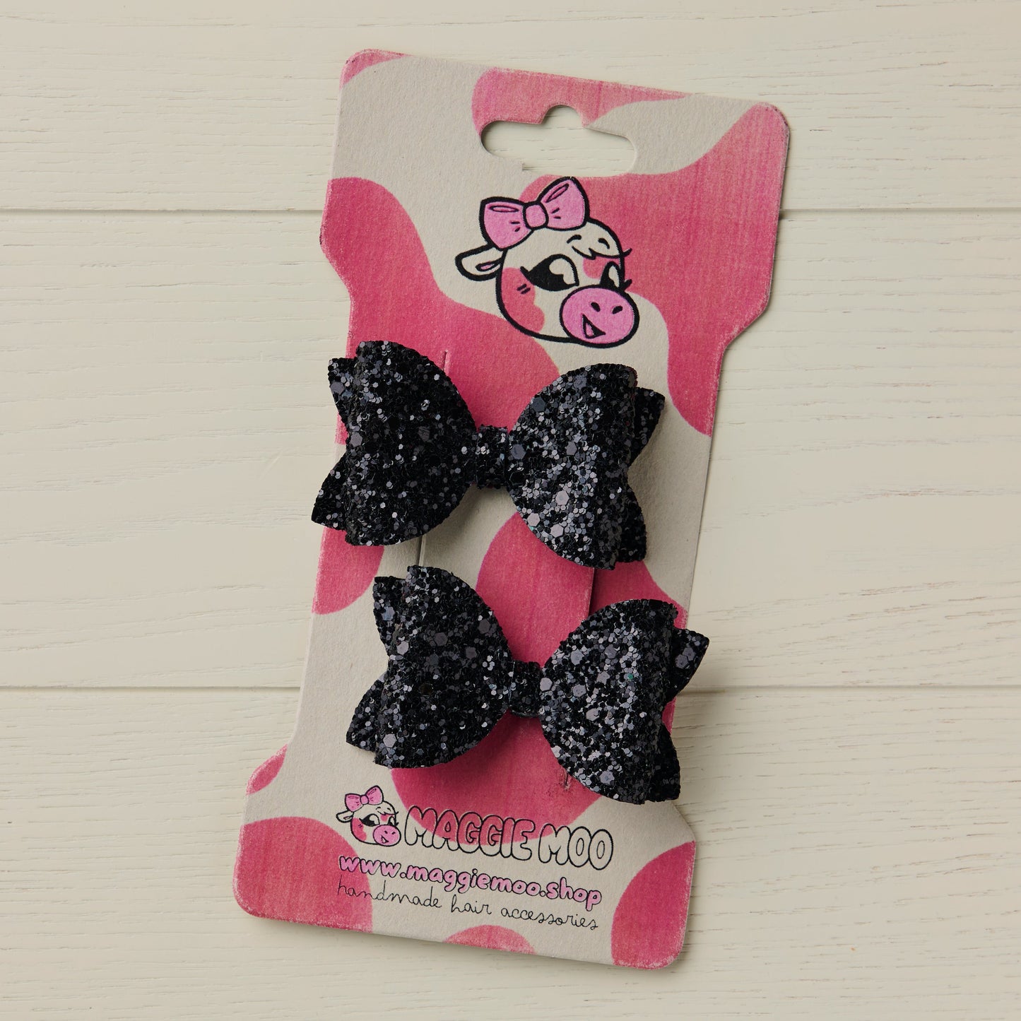 Pair of black glittery hair bows on a display card with a cute cow logo.