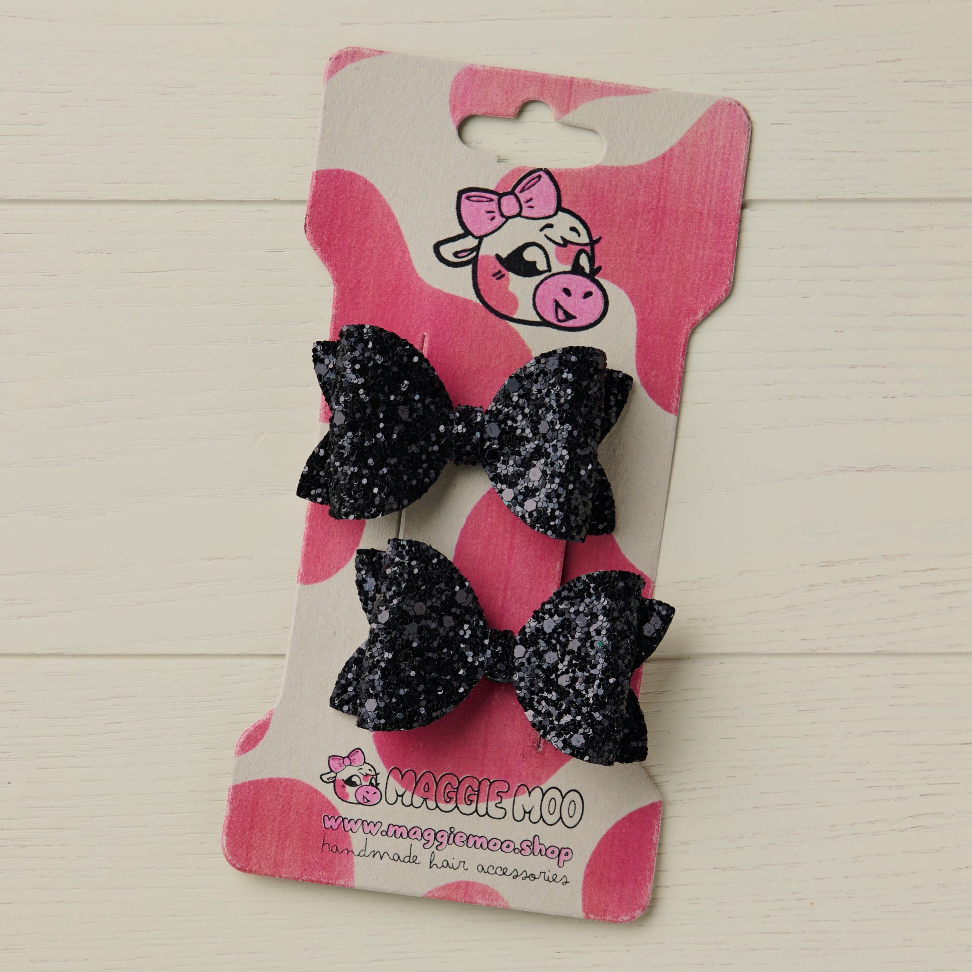 Pair of black glittery hair bows on a display card with a cute cow logo.