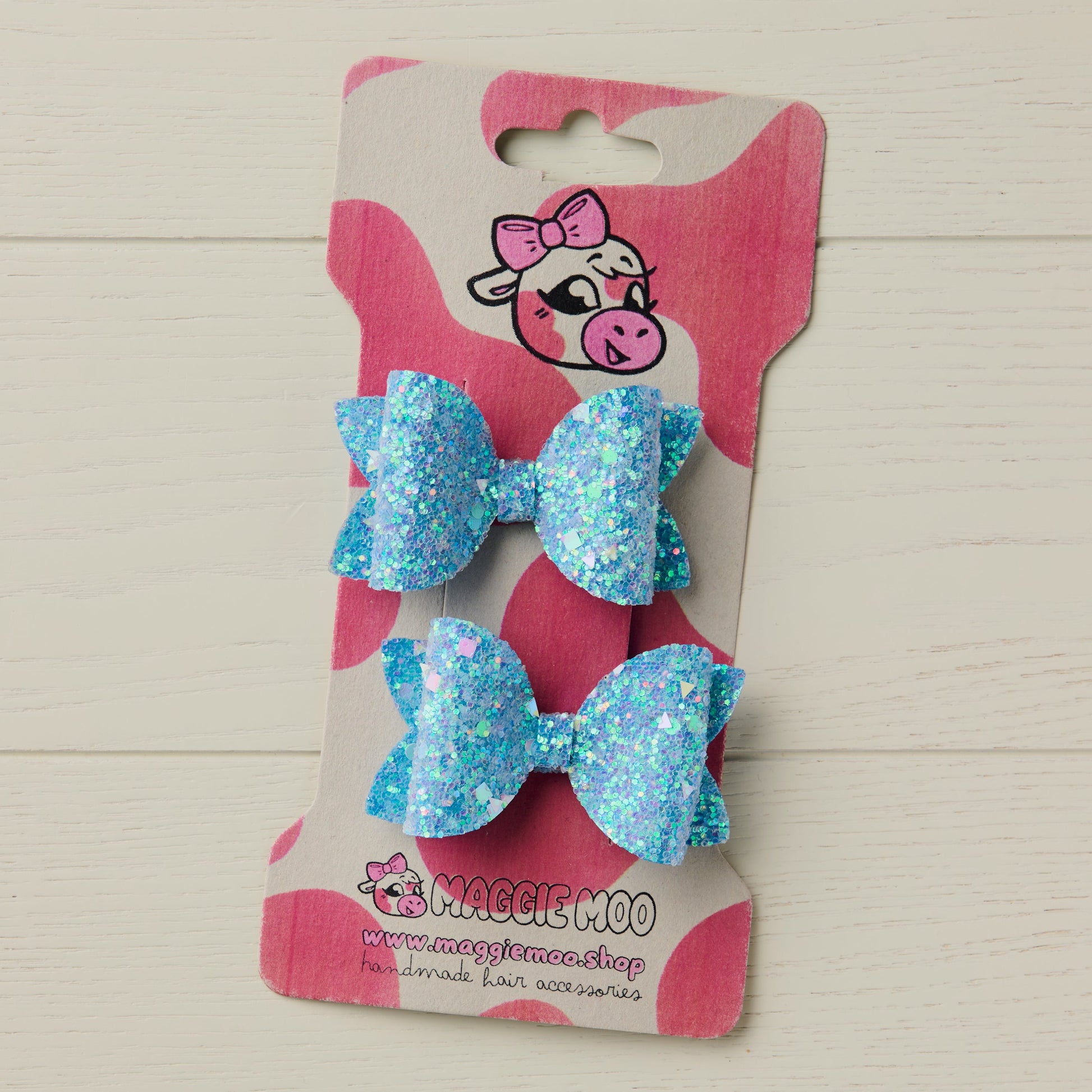 Two Light Blue Chunky Glitter Hair Bows on a display card with a cow logo