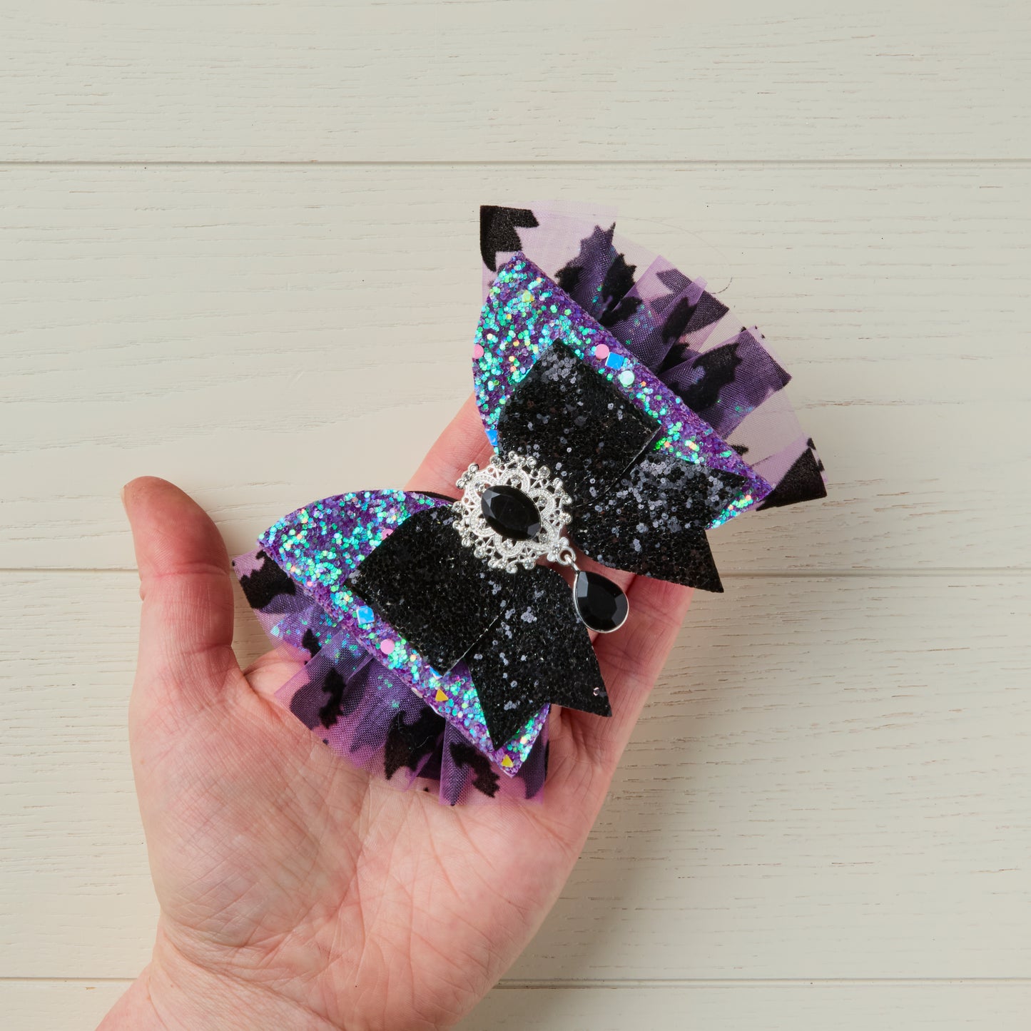 Purple and black Halloween glitter bow on top of palm of a hand to show size reference