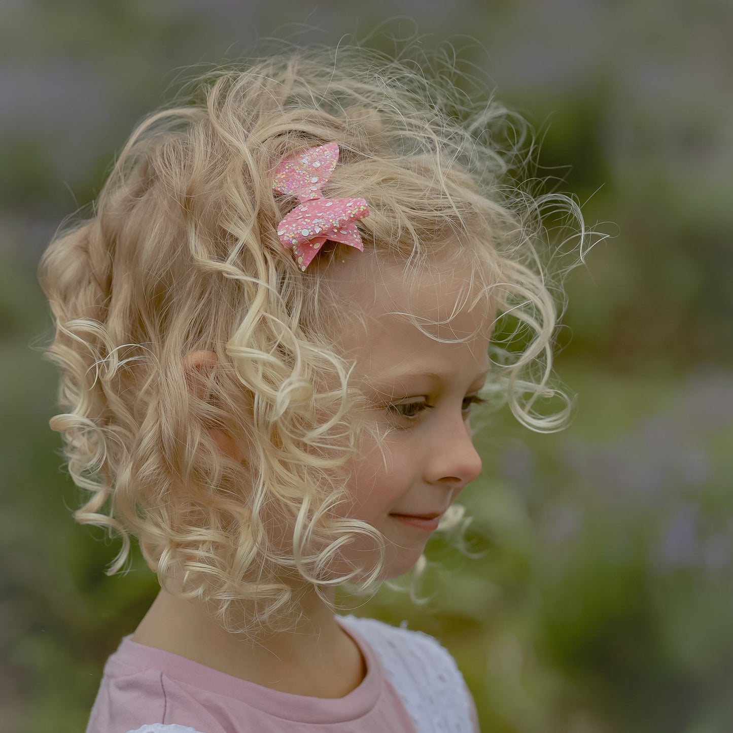 Young girl with curly blonde hair and a pink glitter bow, standing in a field of lavender