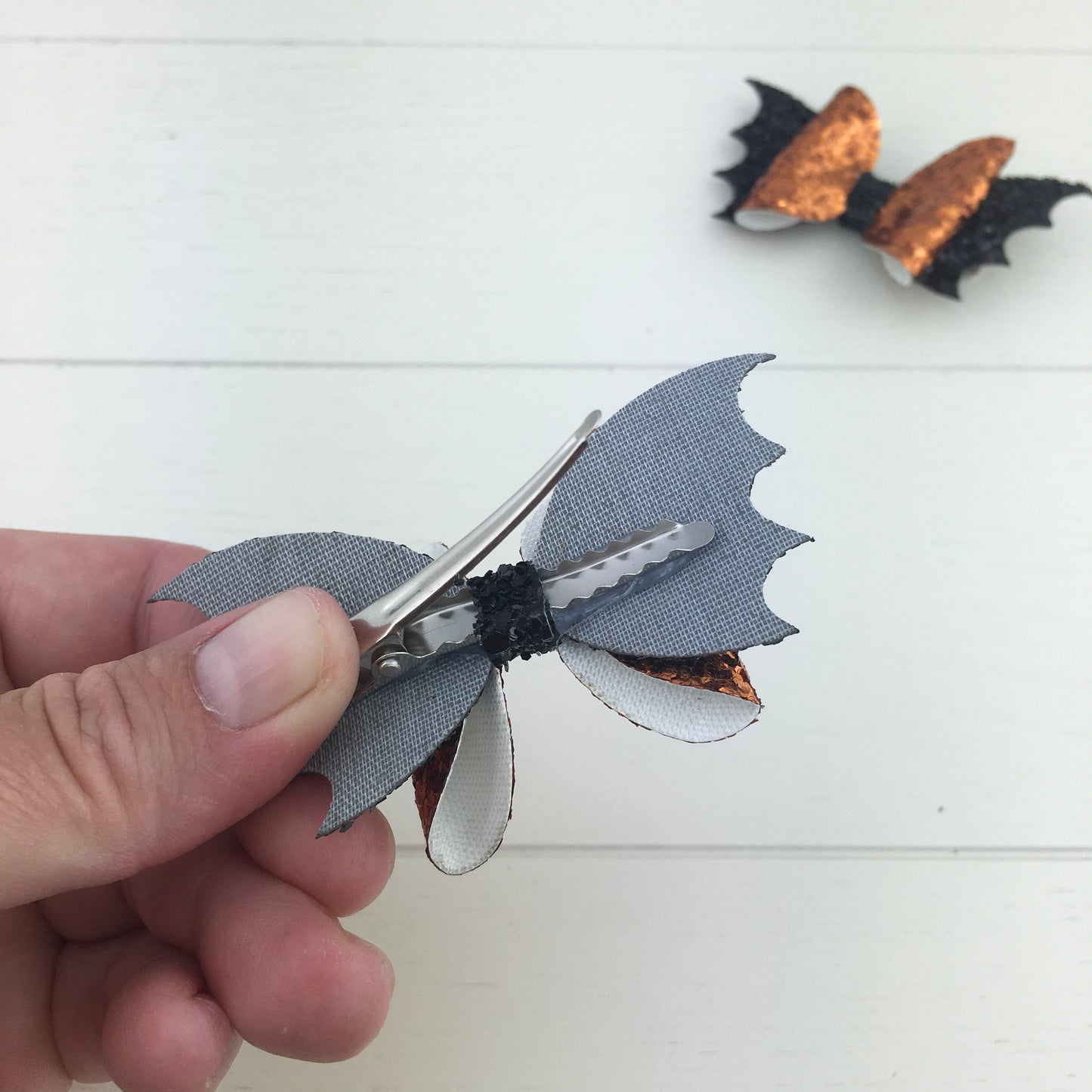 The reverse side of a handmade mini glitter Halloween hair bow, showing the silver, comfy curved alligator clip and the secure attachment of the bow with the centre strip.