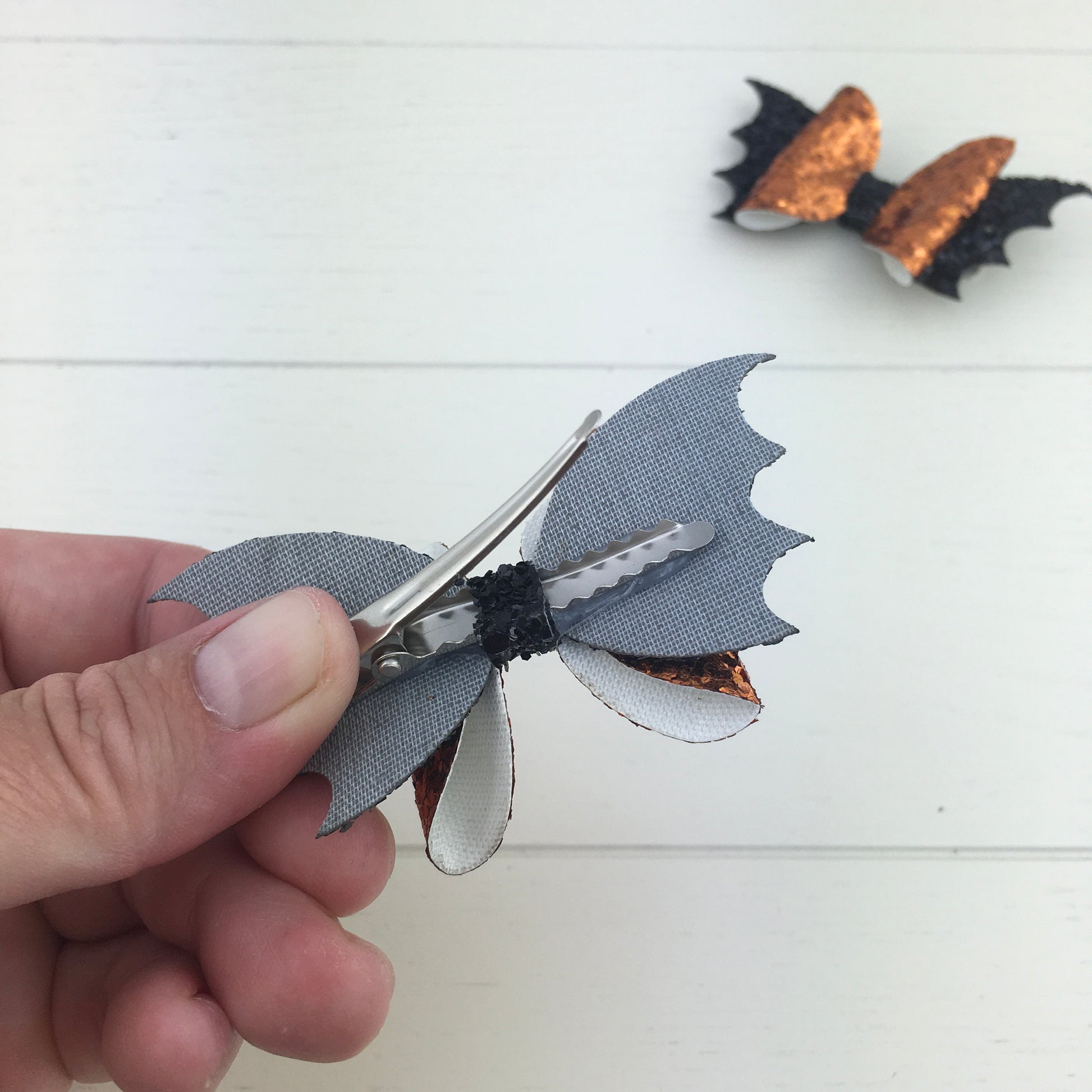 The reverse side of a handmade mini glitter Halloween hair bow, showing the silver, comfy curved alligator clip and the secure attachment of the bow with the centre strip.