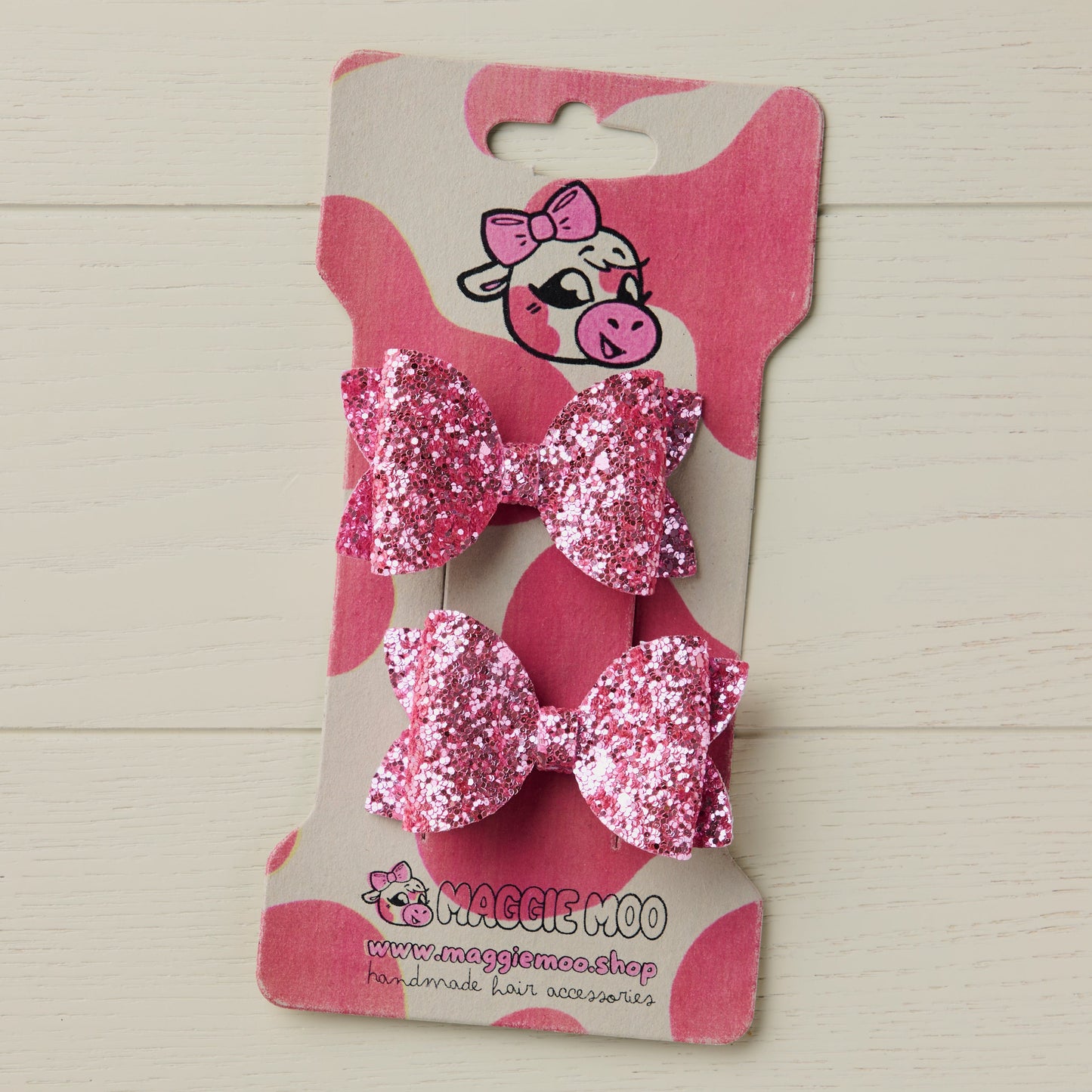 two super sparkly pink glitter bows on a display card with a cute cow logo