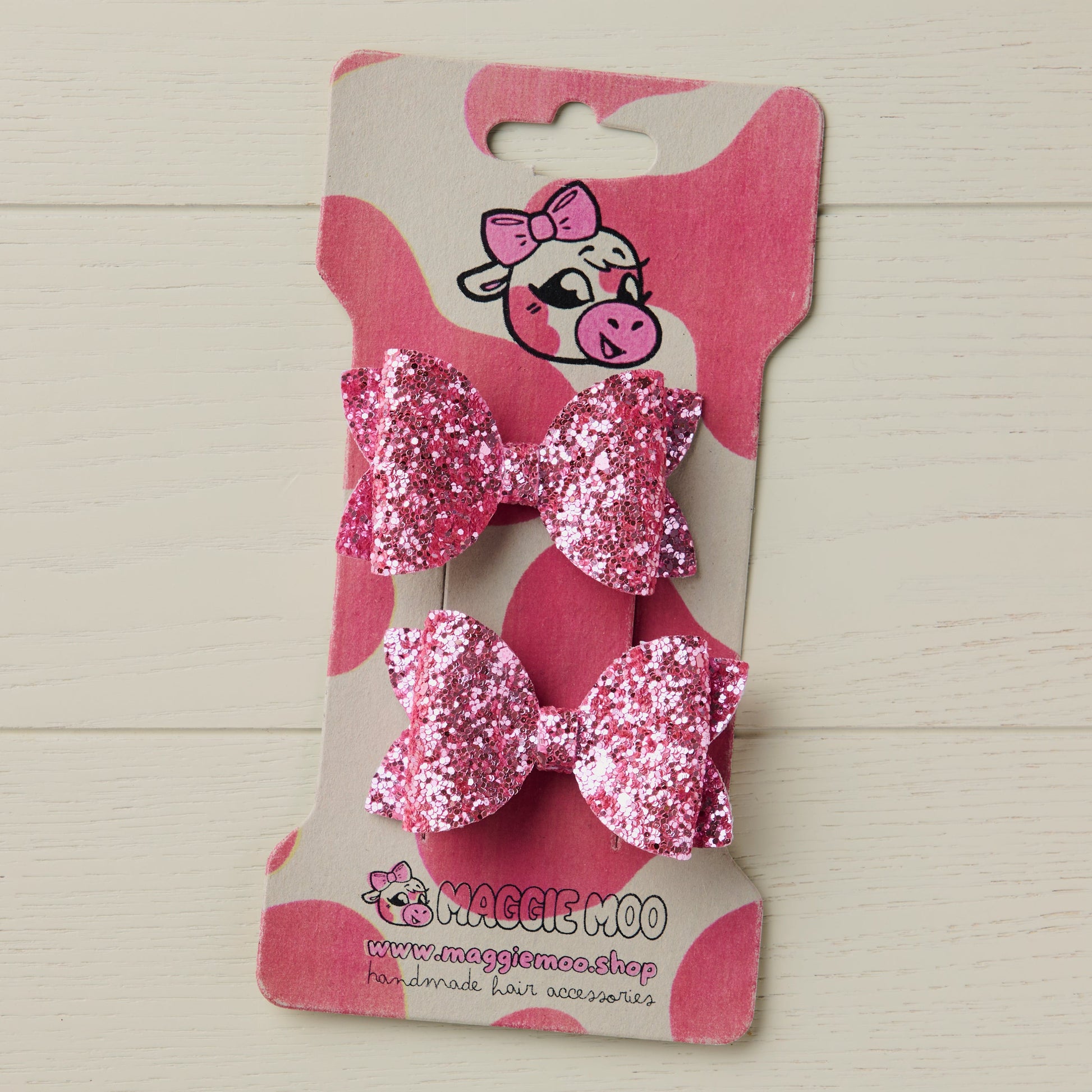 two super sparkly pink glitter bows on a display card with a cute cow logo