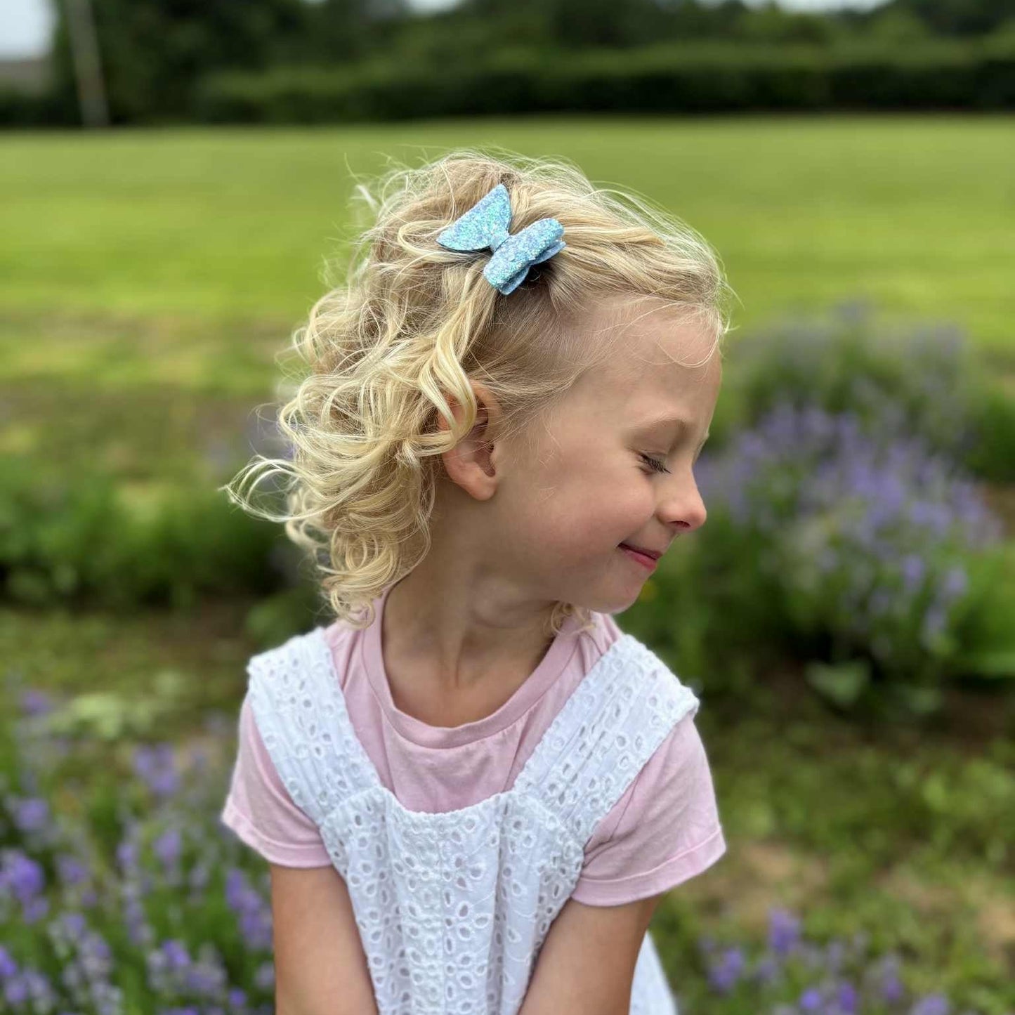 Young girl with a blue glitter bow in her hair standing in a field of lavender.