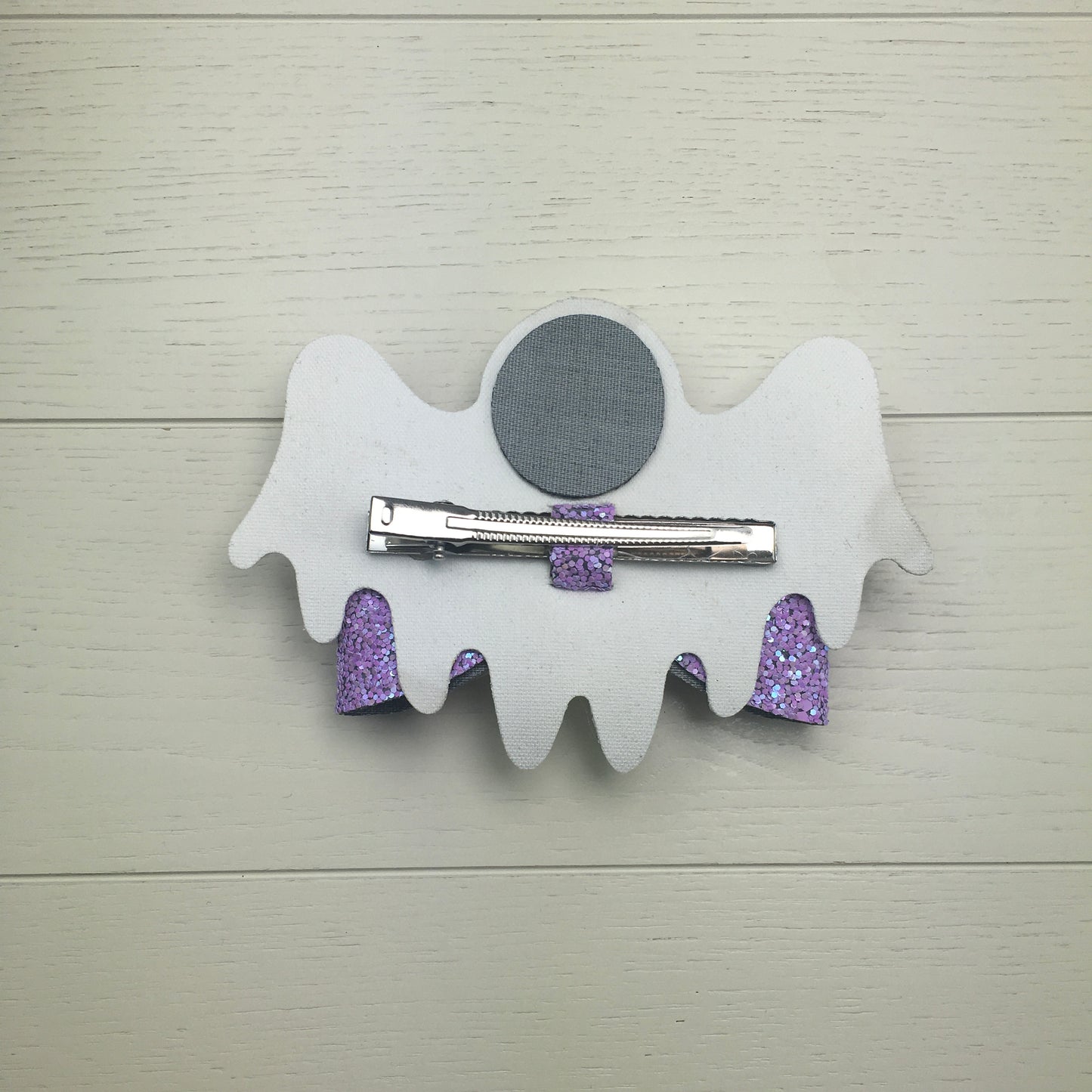 The reverse side of a large ghost shaped Halloween hair bow lying flat on a light wood surface showing the 75mm alligator clip.
