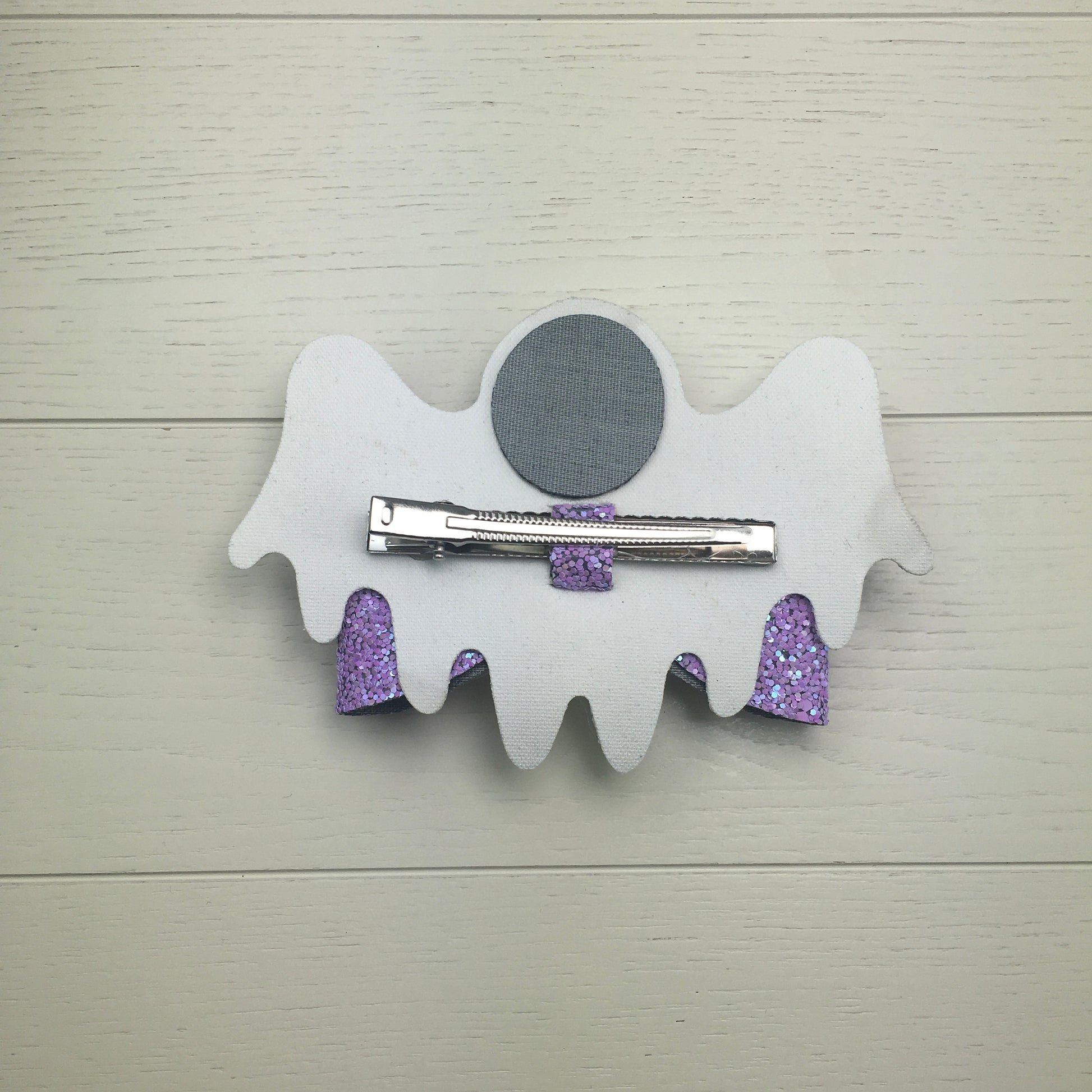 The reverse side of a large ghost shaped Halloween hair bow lying flat on a light wood surface showing the 75mm alligator clip.