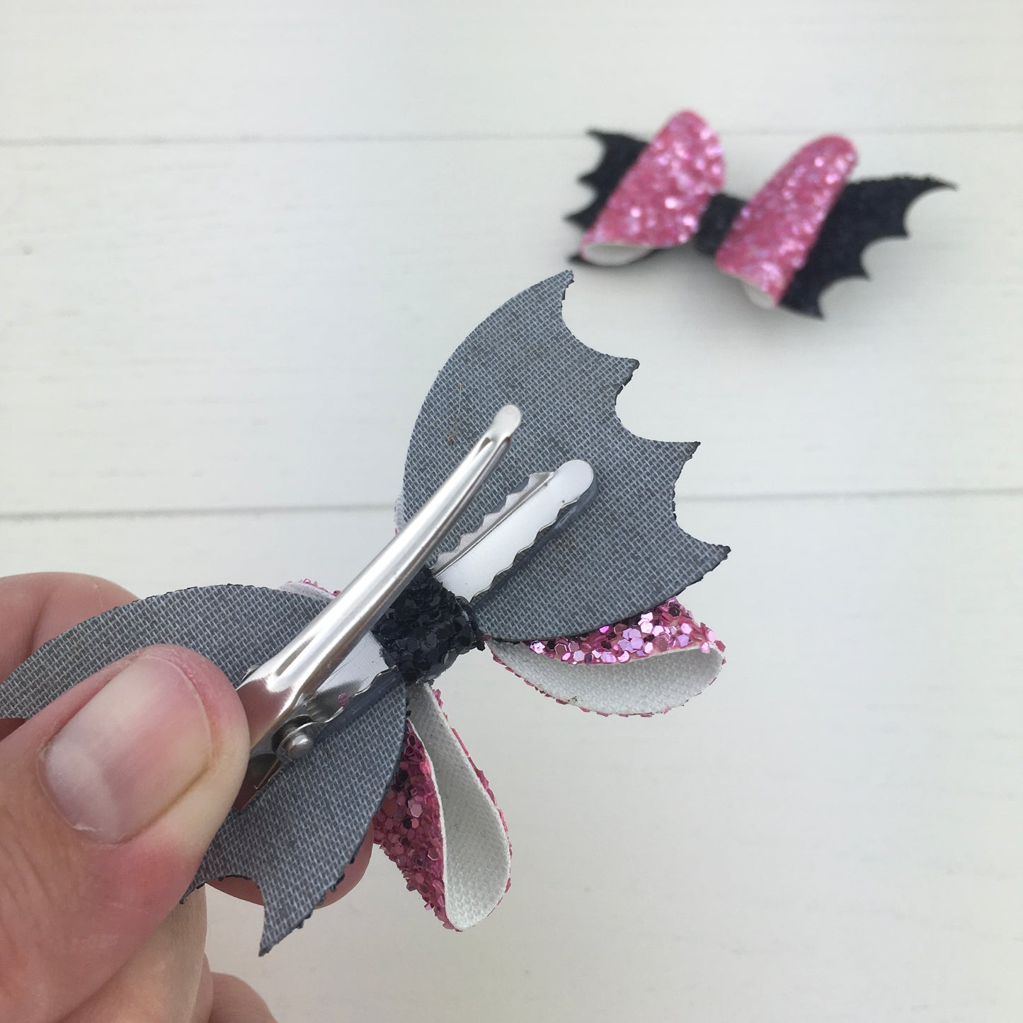 The reverse side of a handmade mini glitter Halloween hair bow, showing the silver, comfy curved alligator clip securely attached with the central strip.