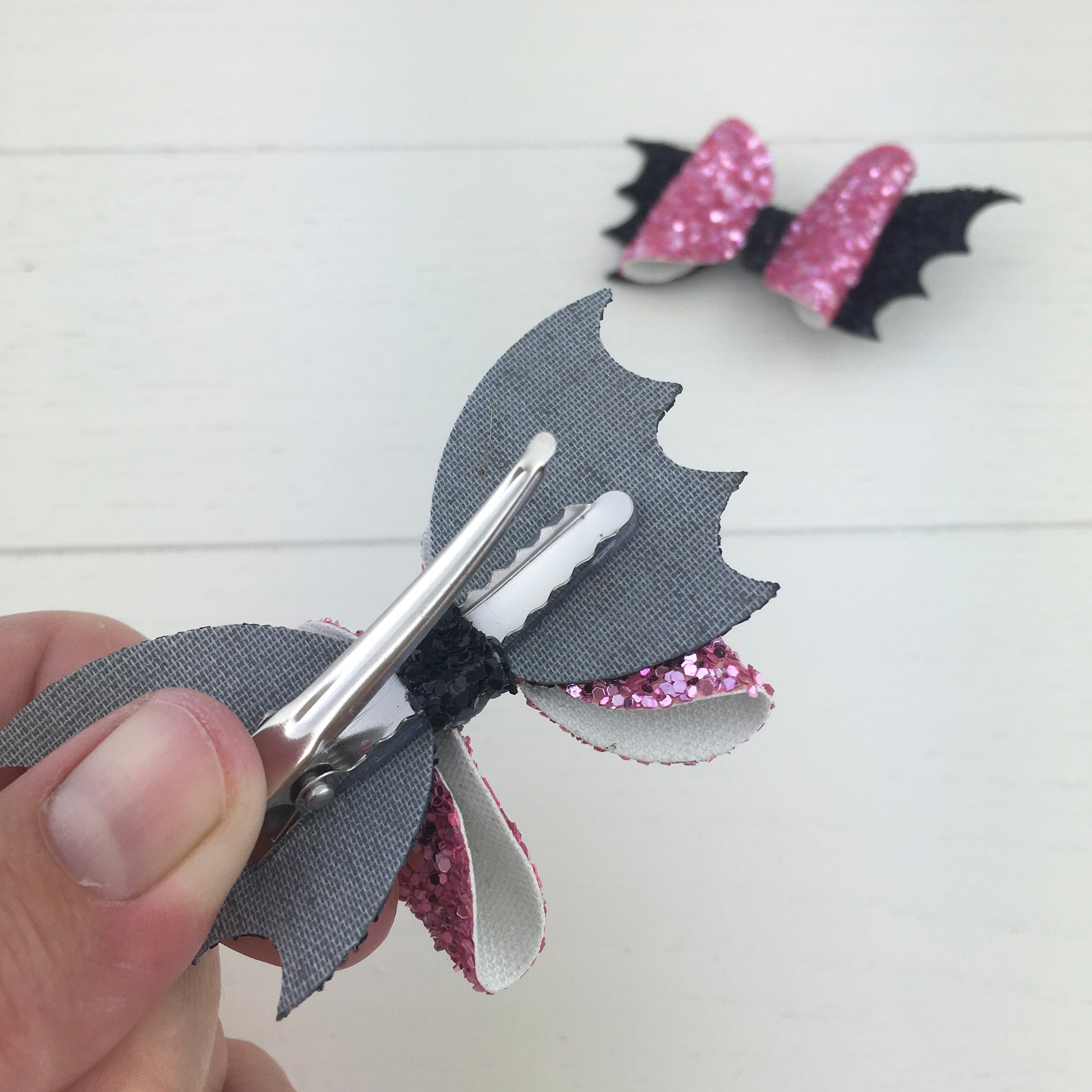 The reverse side of a handmade mini glitter Halloween hair bow, showing the silver, comfy curved alligator clip securely attached with the central strip.