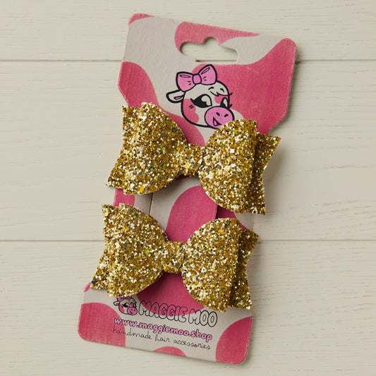 two sparkly gold hair bows on a display card with a cute cow logo