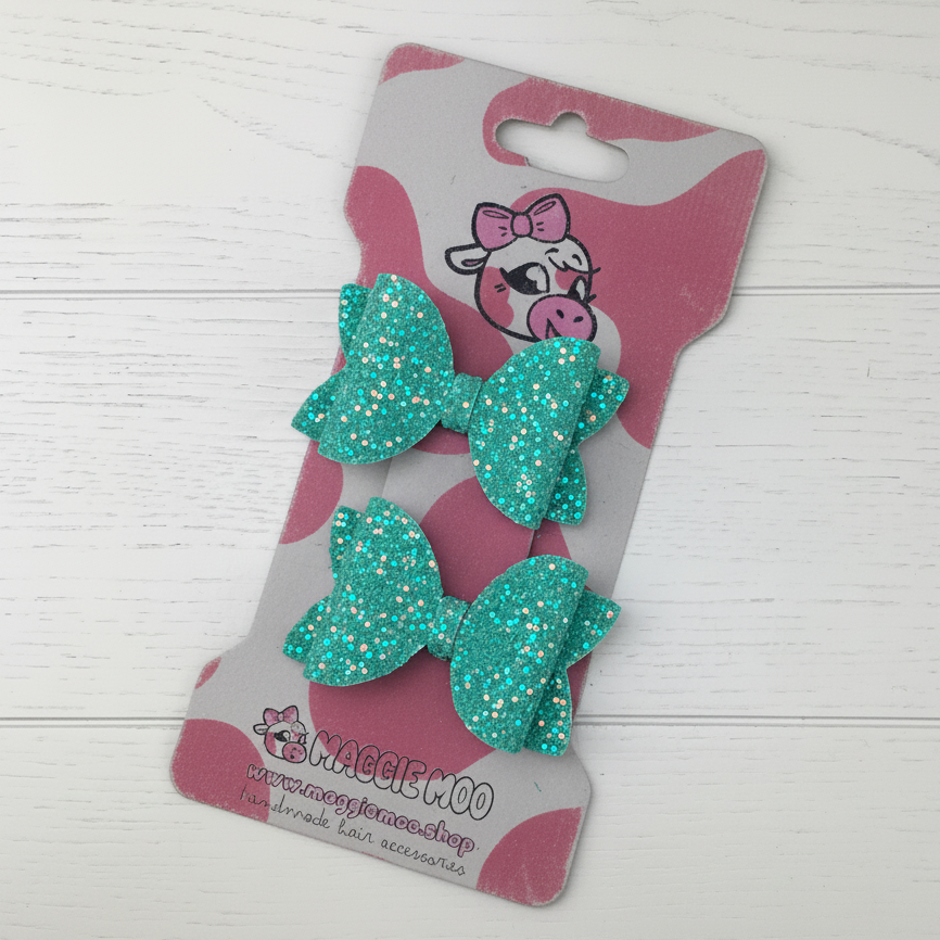 Teal glitter bows on a display card with a cute cow logo