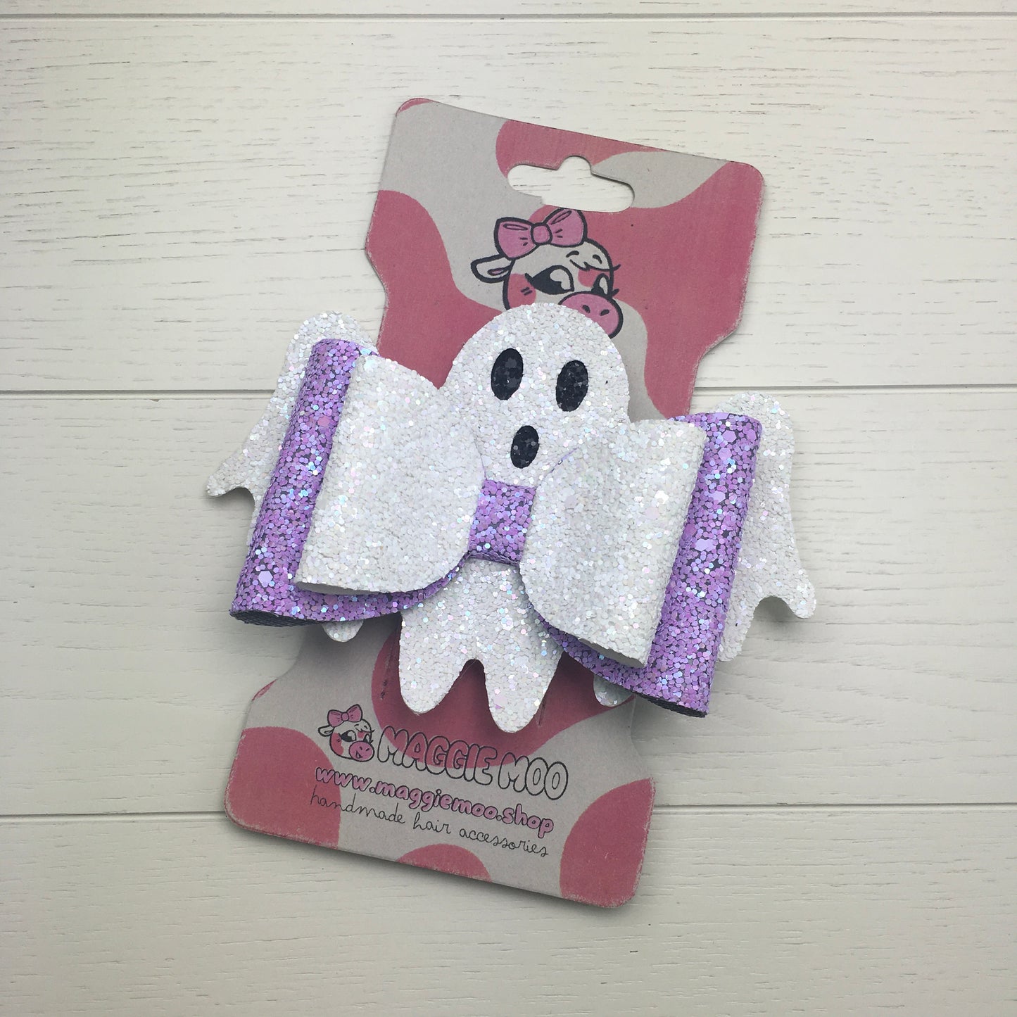 A handmade large lilac and white confetti glitter Halloween hair bow on a recycled card display card with a cute cow logo.