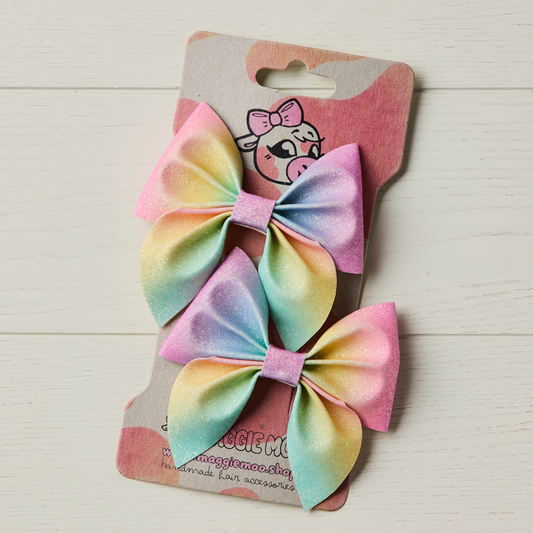 two rainbow glitter hair bows on a display card