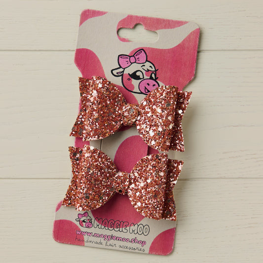 Rose gold glitter hair bows on a display card with a cute cow logo on a light wooden surface