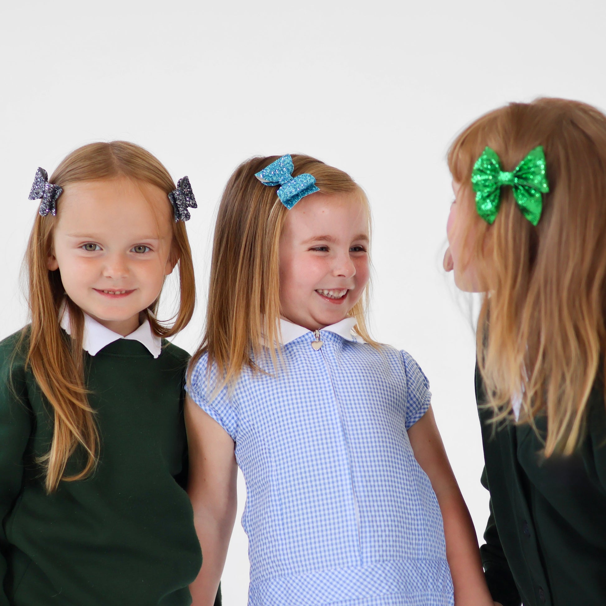 Three girls with sparkly hair bows, wearing school uniforms, on a white background