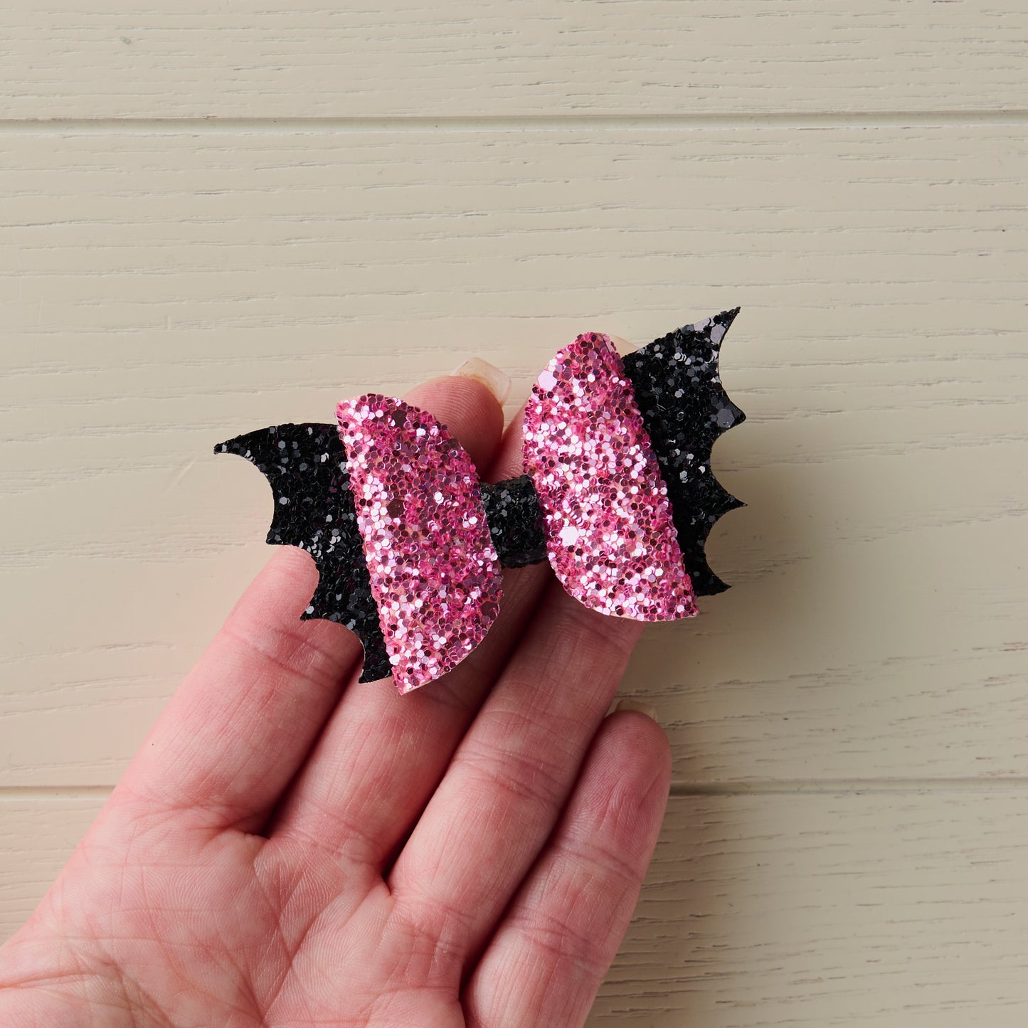 A close-up photo of a small 2.5 inch pink and black sparkly Halloween bat bow placed on top of a human hand to show its size.