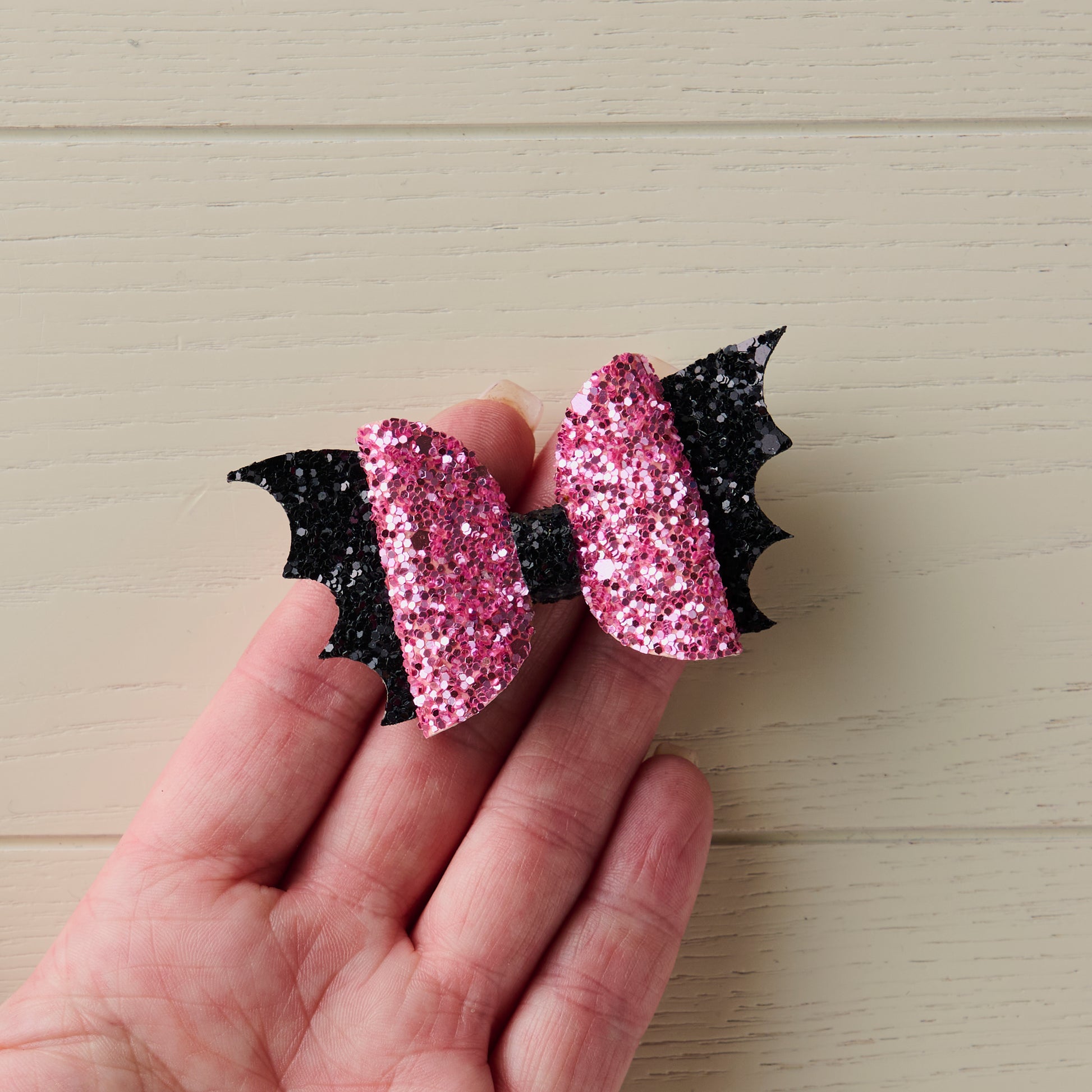 A close-up photo of a small 2.5 inch pink and black sparkly Halloween bat bow placed on top of a human hand to show its size.